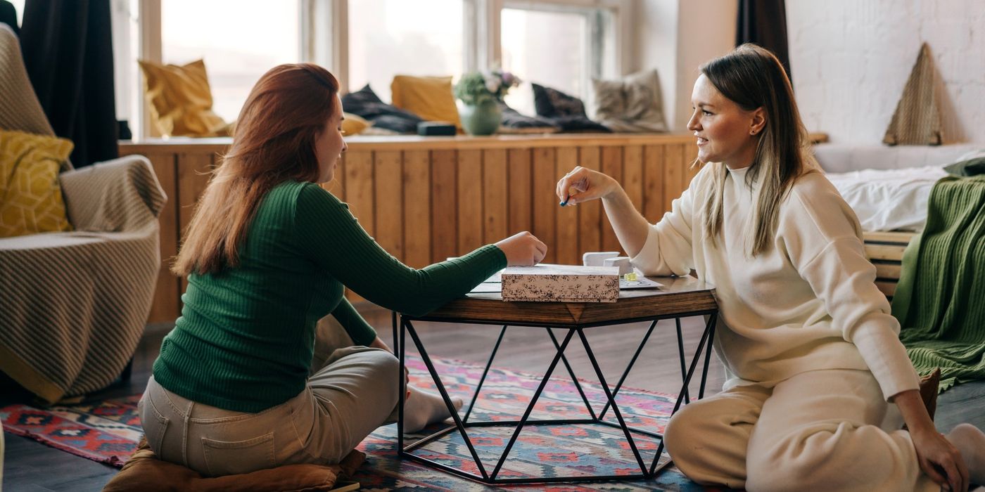 Two women are playing board games at a table inside a home. 