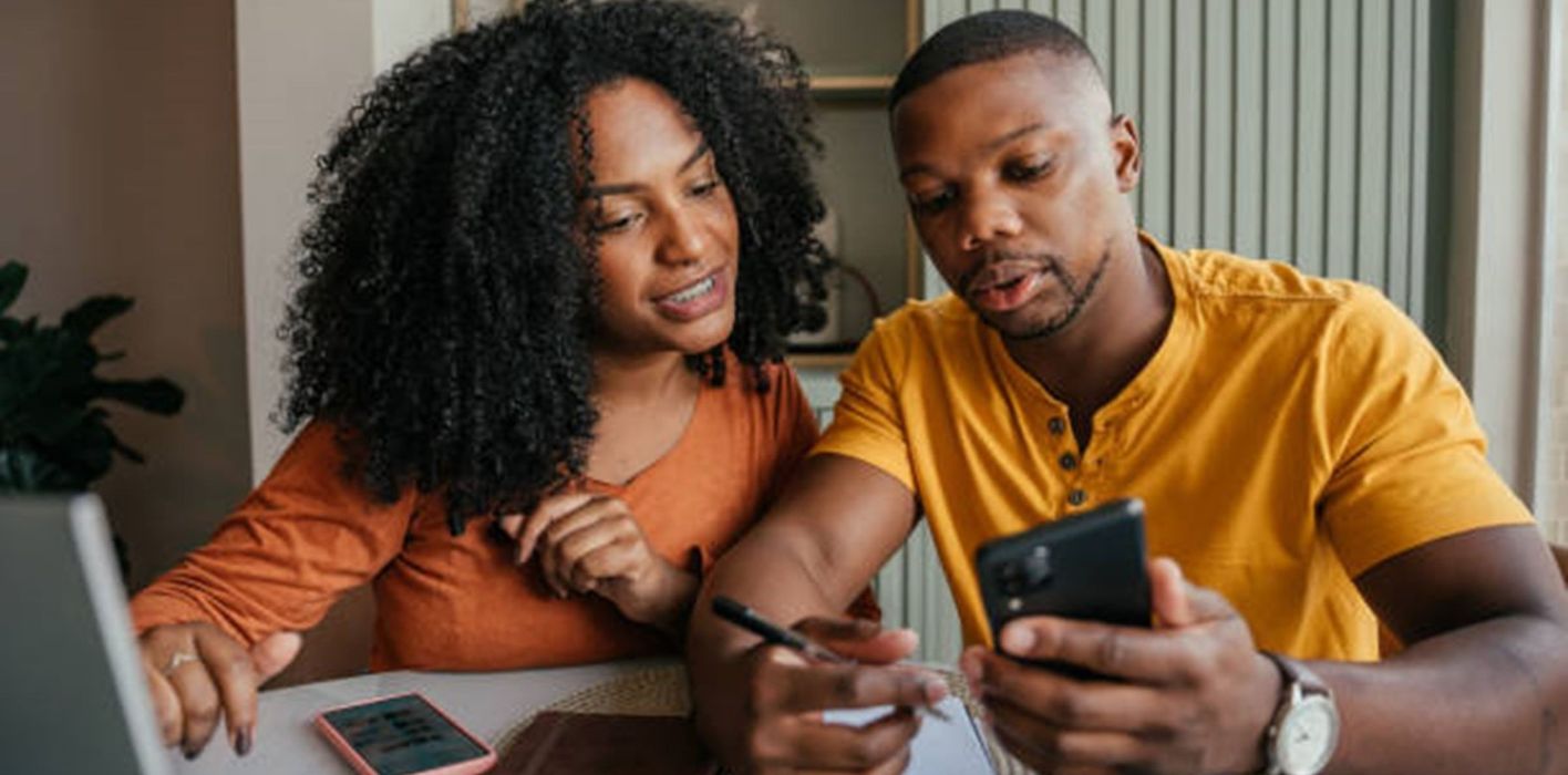 Young couple looking at laptop and phone, taking notes.