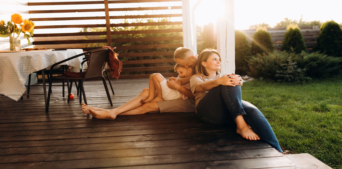 two parents with their young child sitting outside on the porch enjoying the sunset