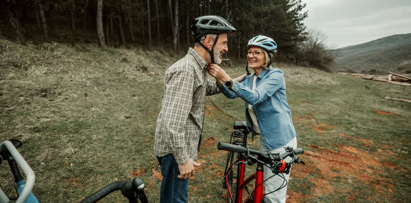 Woman helping her husband to put on cycling helmet before riding in forest