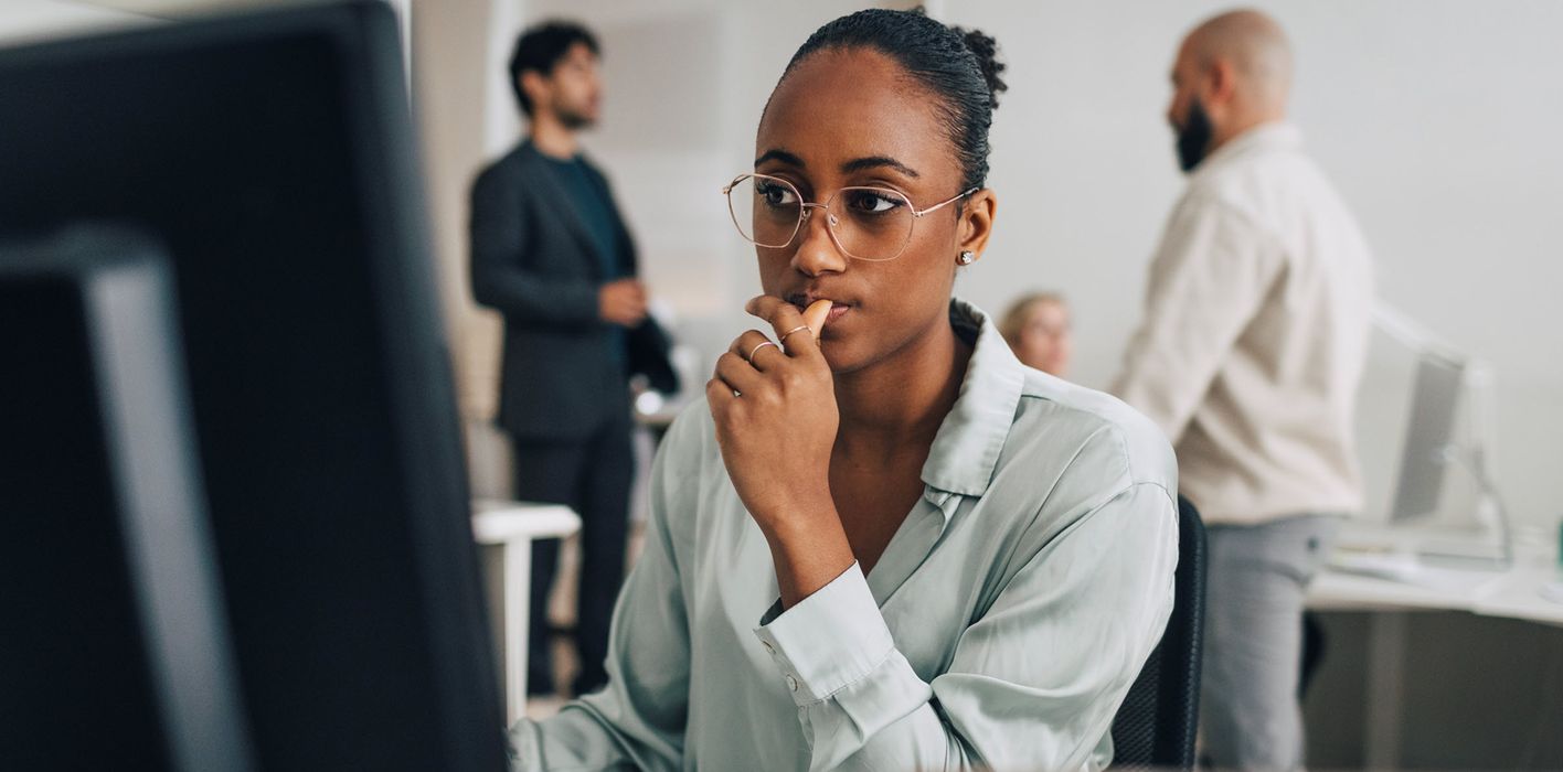 Contemplative young investment professional wearing eyeglasses sitting at desk while working on desktop PC in office reading Northwestern Mutual’s Weekly Market Commentary