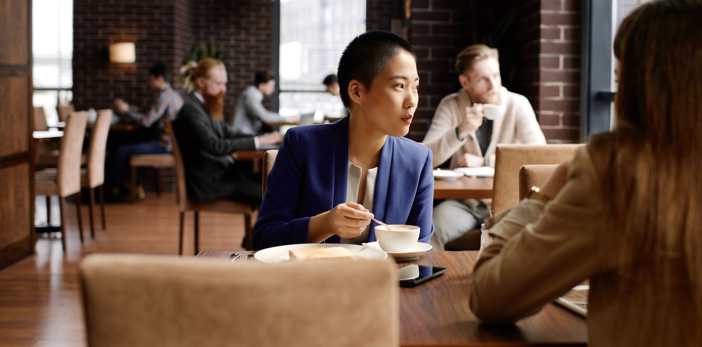 Businesswoman sitting at table in cozy cafe, stirring coffee and assessing the markets and economy white reading Northwestern Mutual’s Weekly Market Commentary