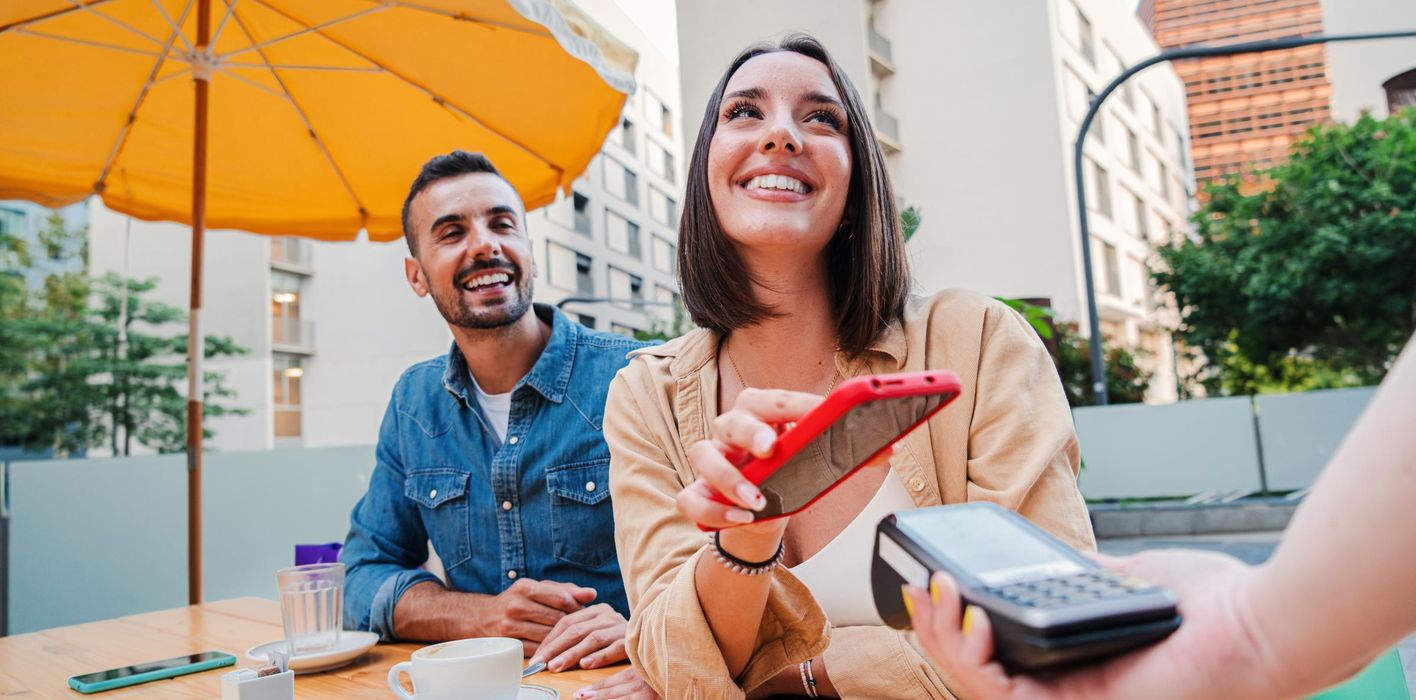 Happy couple paying the bill of the coffee shop using a cellphone contactless payment application.