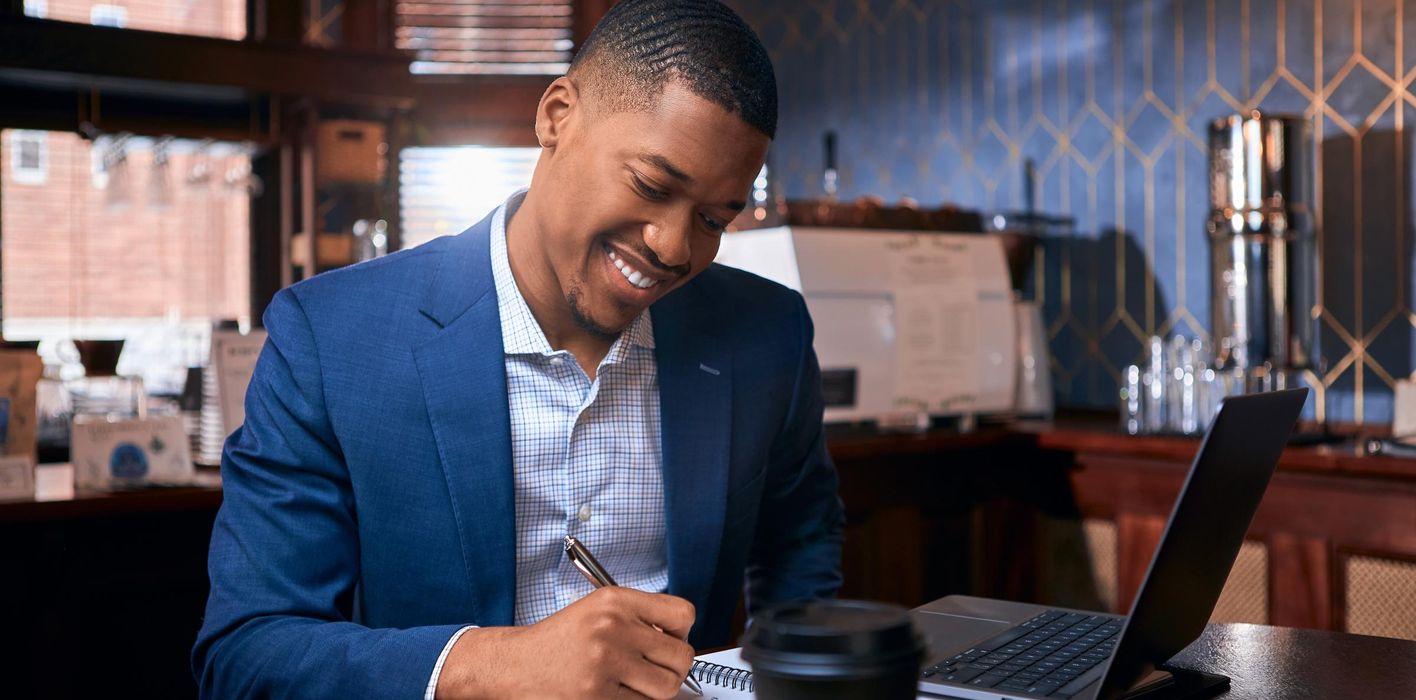 Male advisor smiling and writing notes with laptop