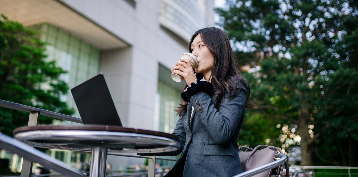 Businesswoman works on laptop outside modern office, analyzing markets and investments