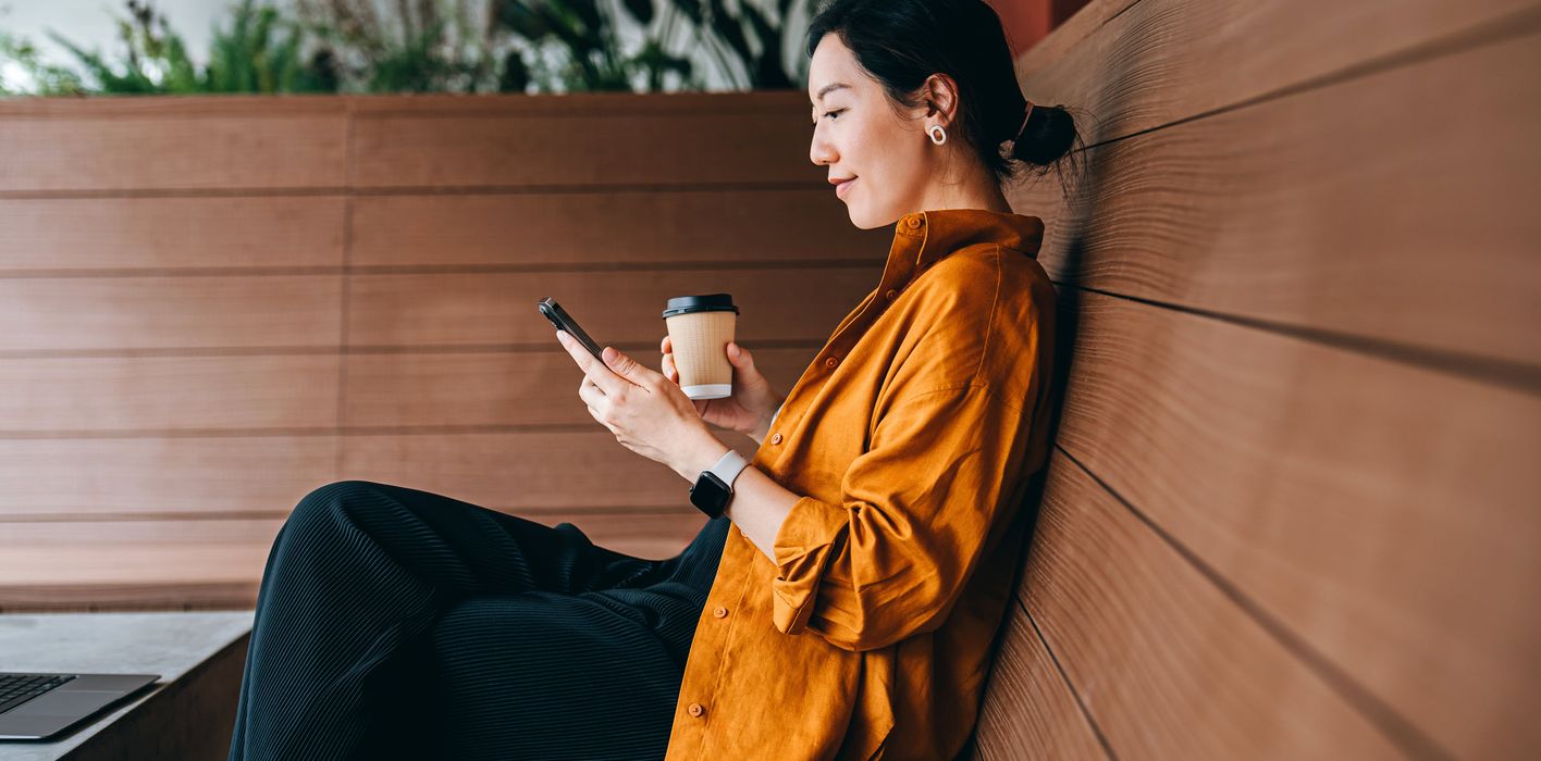 Young woman sitting in a sidewalk cafe with a cup of coffee and using her smartphone.