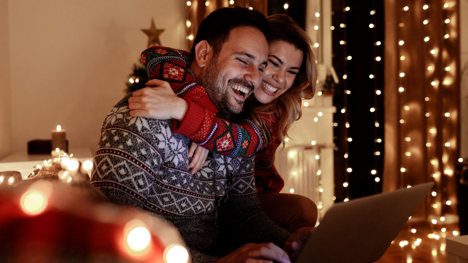 Couple in Christmas sweaters on a couch looking at a laptop learning how to improve their finances in December