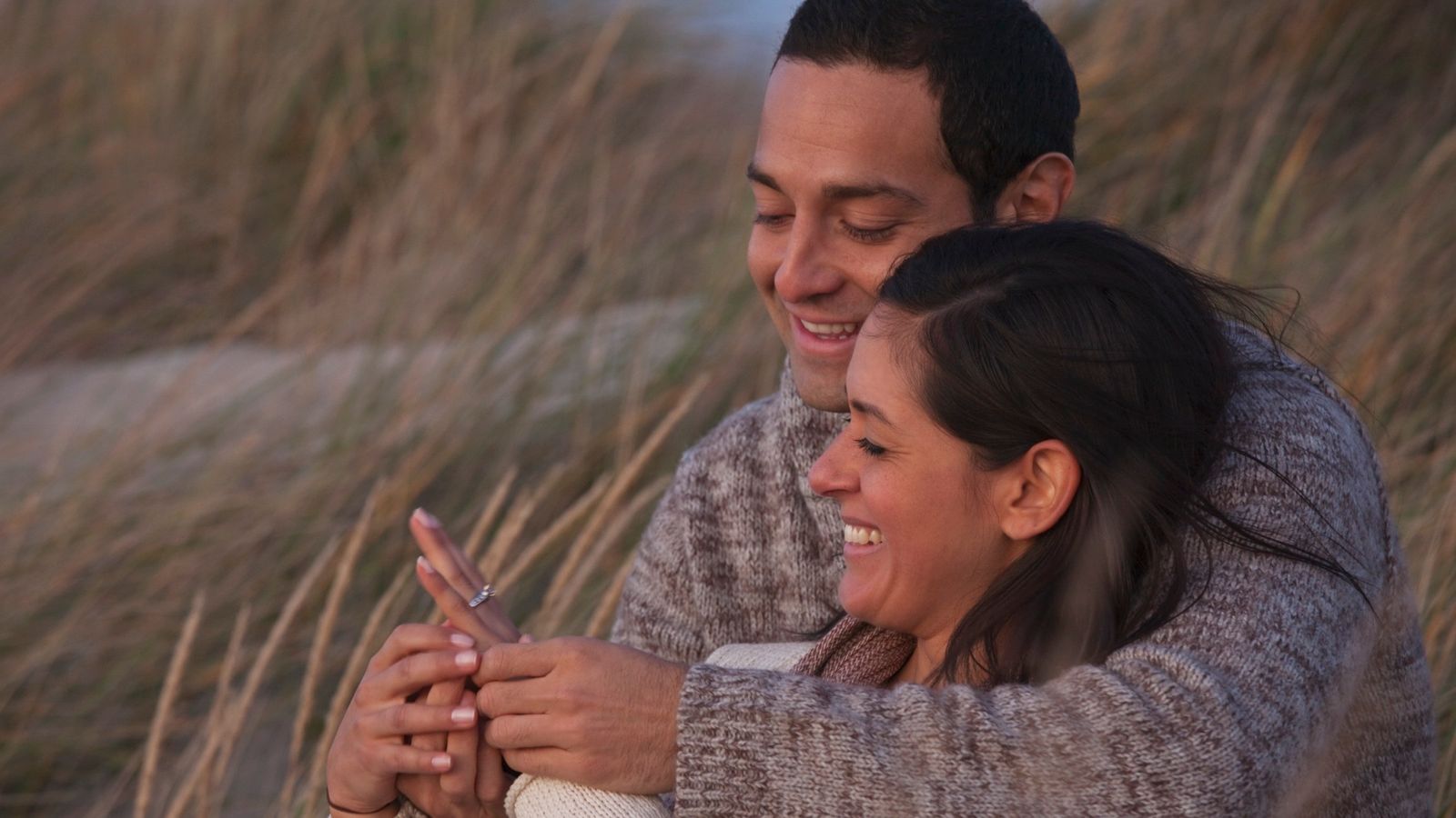 Couple sitting together smiling looking at an engagement ring