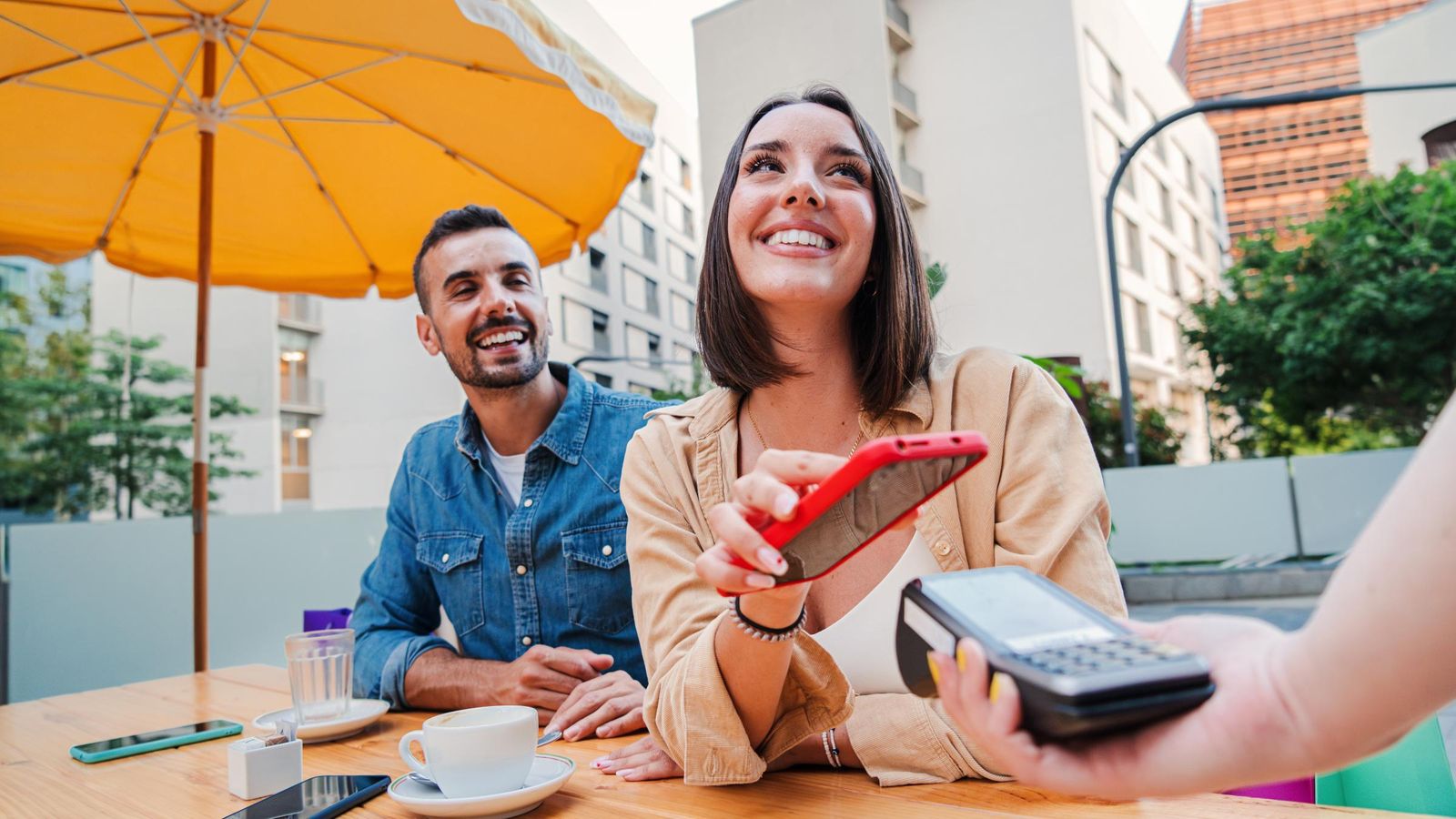Happy couple paying the bill of the coffee shop using a cellphone contactless payment application.