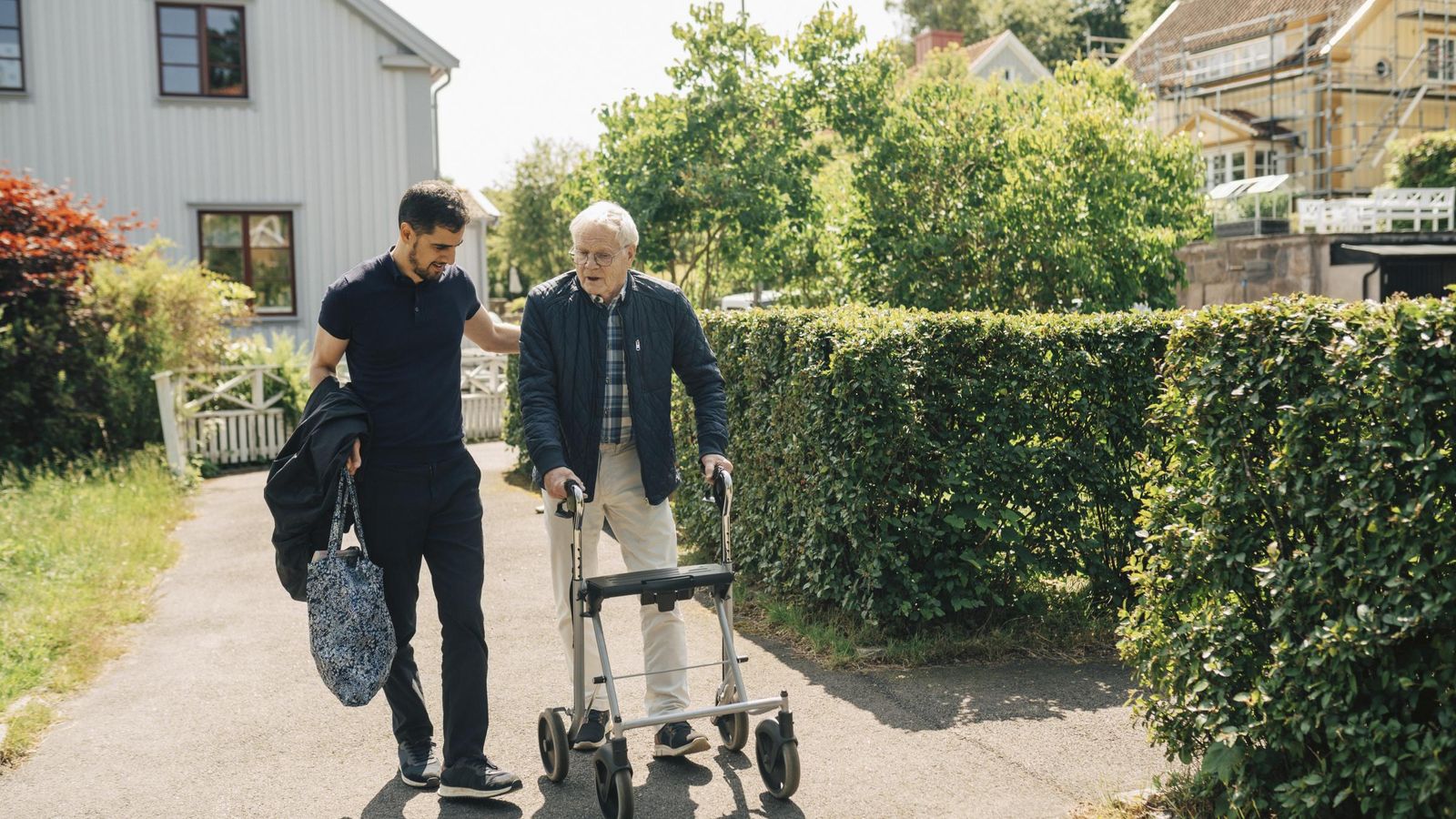 Male caregiver walking with senior man using rollator in park at sunny day