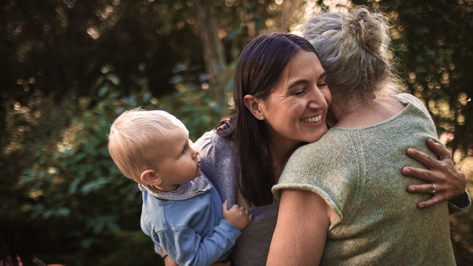 Happy woman with baby boy hugging senior mother in garden