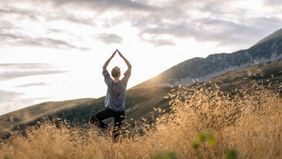 Woman doing yoga in the mountains while thinking about financial wellness.