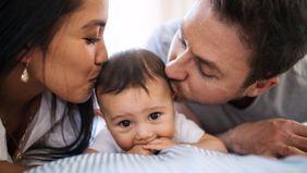 Couple on a bed kissing their baby