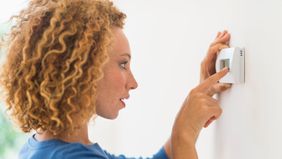 woman setting temperature on thermostat