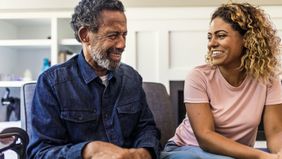 An elderly father and his daughter talk to eachother on the couch