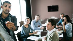 Man writing long-term business goals on board in conference room full of coworkers