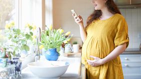 pregnant woman looking at phone next to kitchen sink