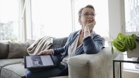 Woman on couch with tablet showing a family photo.