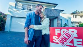 Couple standing in front of a home with for-sale sign.