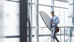 Executive with his surfboard at the office as he navigates his unlimited PTO policy