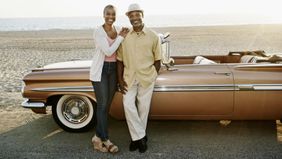 Couple standing next to convertible on beach