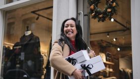 Woman smiling while holding gift boxes outside a store during holiday shopping