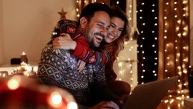 Couple in Christmas sweaters on a couch looking at a laptop learning how to improve their finances in December