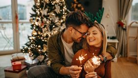 Couple holding sparklers and looking at each other in front of a Christmas tree making their financial New Year’s resolutions.