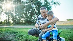 A grandparent and grandchild fish together at the lakeshore.