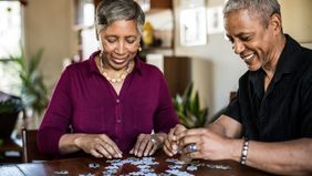 Two 60-year-olds assemble a puzzle at home.