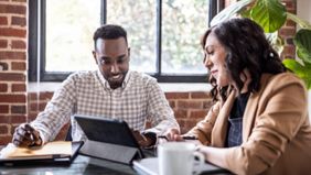 Two people smiling while discussing file on digital tablet