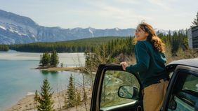 Woman looking at scenic lake along the road in Banff during road trip with SUV in springtime