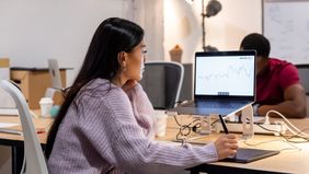 Woman tracks economic and market movements on her computer in a modern office.