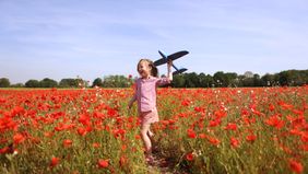 A girl playing with a plane in a field of flowers