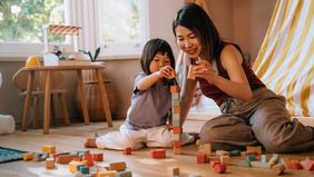 Mother and her daughter having fun, playing with toys together in the bedroom.