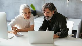Two colleagues in modern office, reading information on laptops