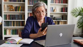 Woman contemplates financial returns on laptop in book-lined office