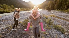 Grandfather and father carrying children piggyback at a riverbank at sunset