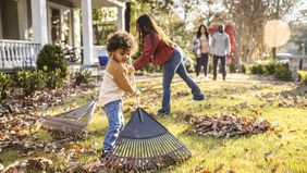 Children raking leaves in front yard of home
