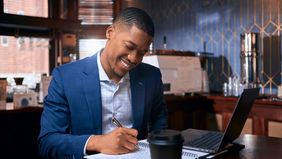 Male advisor smiling and writing notes with laptop