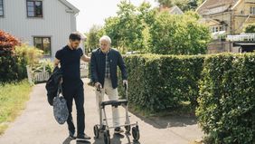 Male caregiver walking with senior man using rollator in park at sunny day