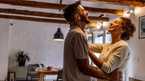 joyful couple shares a warm hug and big smile in a bright, cozy living space, conveying love, connection, and positive energy in a home environment.