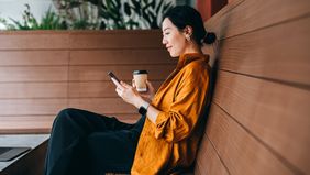 Young woman sitting in a sidewalk cafe with a cup of coffee and using her smartphone.