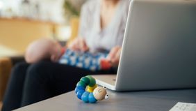 Mom playing with baby while working at home on laptop.