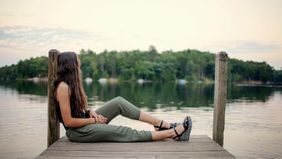 woman sitting on dock looking at lake
