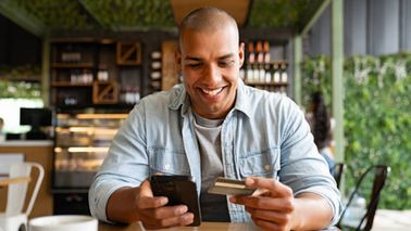 Man at a cafe shopping on his cell phone and paying by debit card.