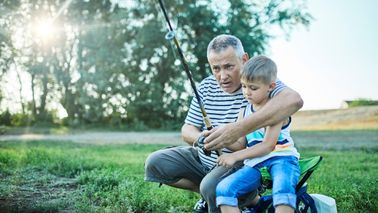 A grandparent and grandchild fish together at the lakeshore.