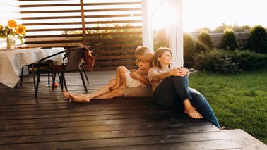 two parents with their young child sitting outside on the porch enjoying the sunset