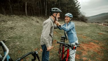 Woman helping her husband to put on cycling helmet before riding in forest