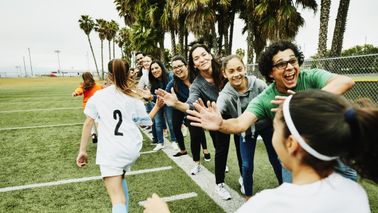Young female soccer players high fiving parents on sidelines after soccer game